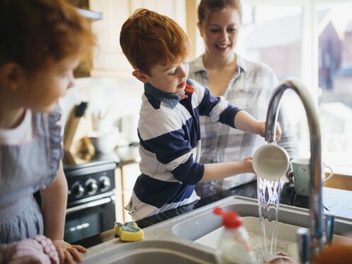 Two children and their Mother washing the dishes in the kitchen sink.